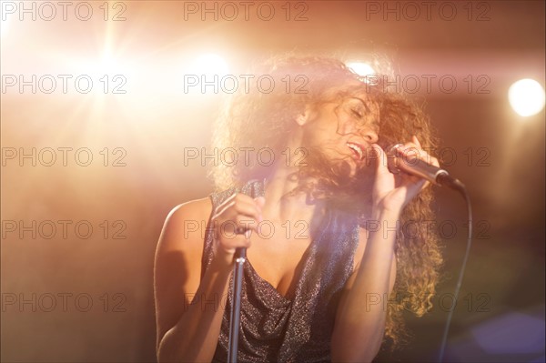 Young woman singing in spotlight.