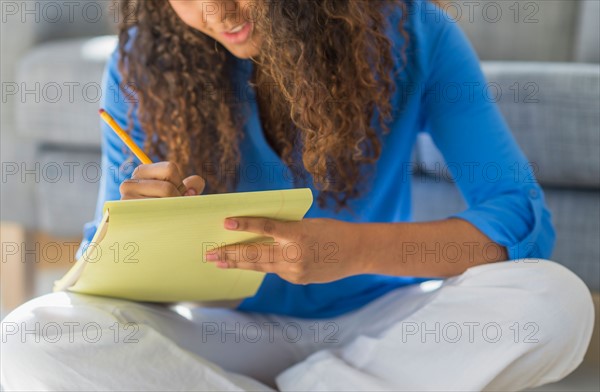 Young woman writing in yellow notepad.