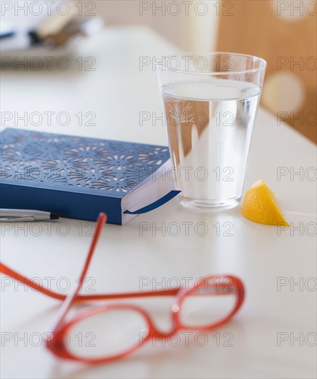 View of spectacles, personal organizer and glass of water on table