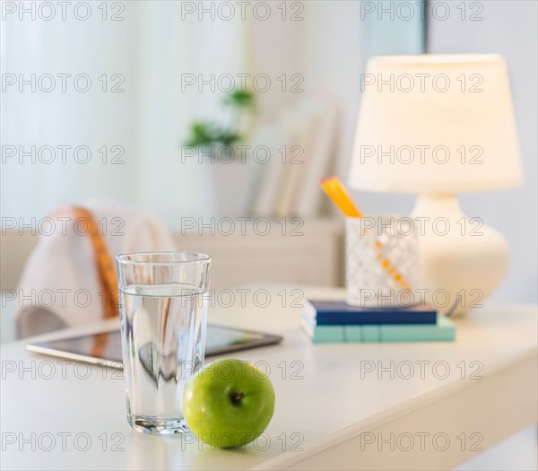 View of glass of water, apple and digital tablet on table