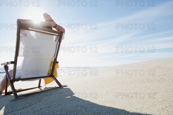 Rear view of woman relaxing on chair at beach