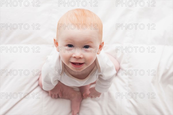 Directly above portrait of baby boy (18-23 months) sitting on duvet and looking at camera