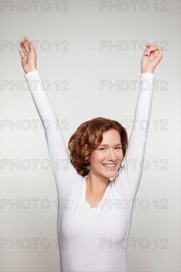 Studio shot portrait of young woman in white blouse with arms raised