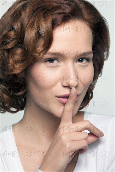Studio shot portrait of young woman in white blouse with finger on lips