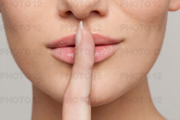 Studio shot portrait of young woman in white blouse with finger on lips