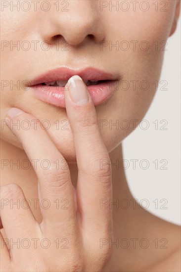 Studio shot portrait of young woman in white blouse with finger on lips