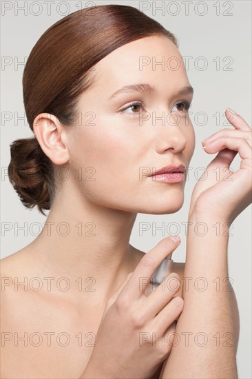 Studio shot portrait of young woman holding perfume