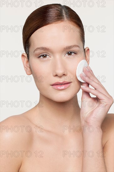 Studio shot portrait of young woman purifying her face with cotton pad