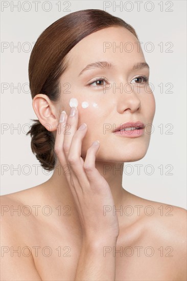 Studio shot of young woman applying moisturizer on face