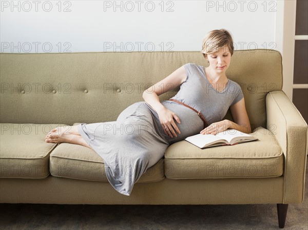 Pregnant woman lying on sofa reading