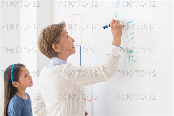 Teacher and schoolgirl (8-9) writing at whiteboard.