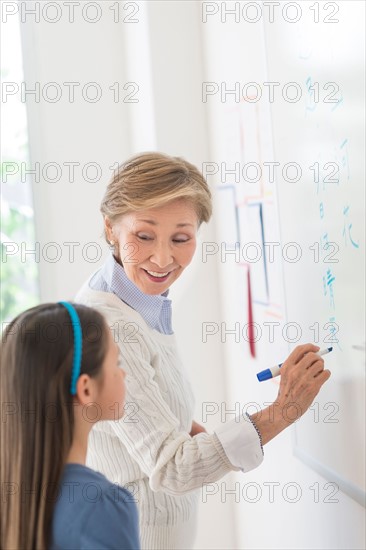 Teacher and schoolgirl (8-9) writing at whiteboard.