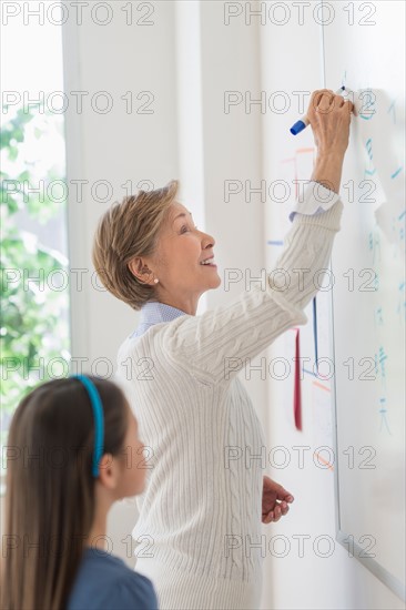 Teacher and schoolgirl (8-9) writing at whiteboard.