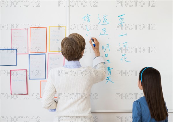 Teacher and schoolgirl (8-9) writing at whiteboard.