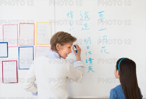 Teacher and schoolgirl (8-9) writing at whiteboard.