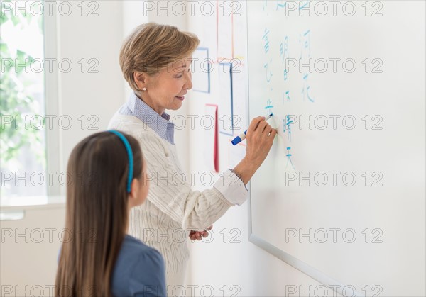 Teacher and schoolgirl (8-9) writing at whiteboard.