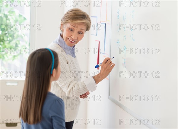 Teacher and schoolgirl (8-9) writing at whiteboard.