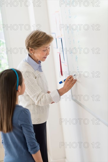 Teacher and schoolgirl (8-9) writing at whiteboard.