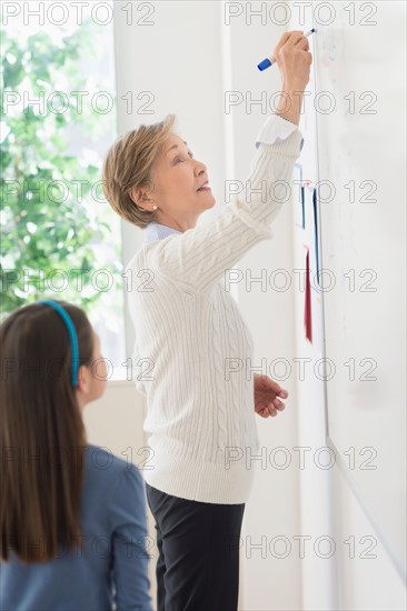 Teacher and schoolgirl (8-9) writing at whiteboard.