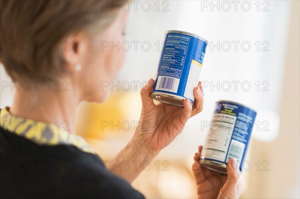 Senior woman reading labels on canned food.