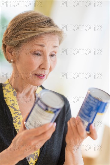 Senior woman reading labels on canned food.