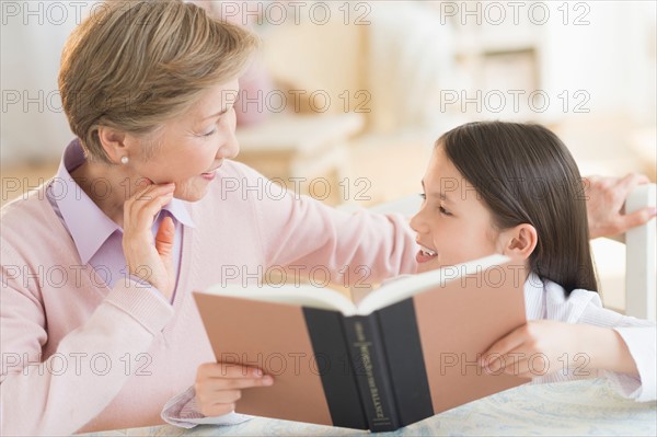 Granddaughter (8-9) and grandmother reading book.