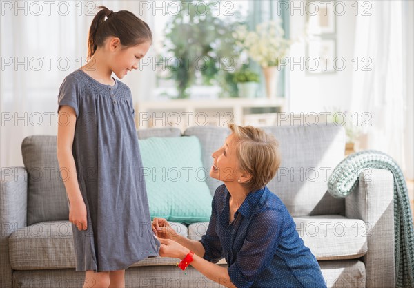 Grandmother attaching sewing pins to granddaughter's (8-9) dress.