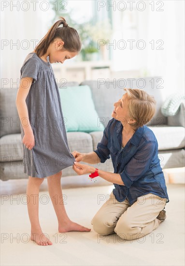 Grandmother attaching sewing pins to granddaughter's (8-9) dress.