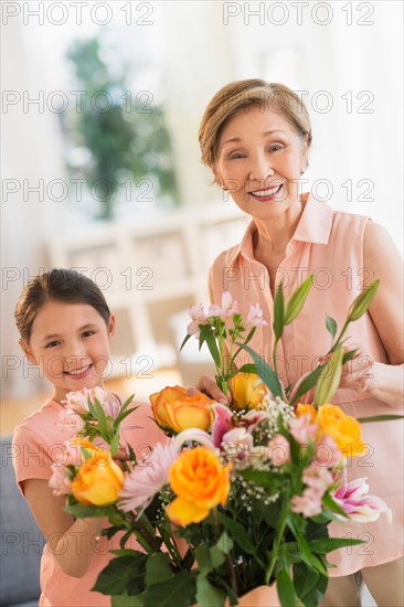 Granddaughter (8-9) and grandmother arranging flowers at home.