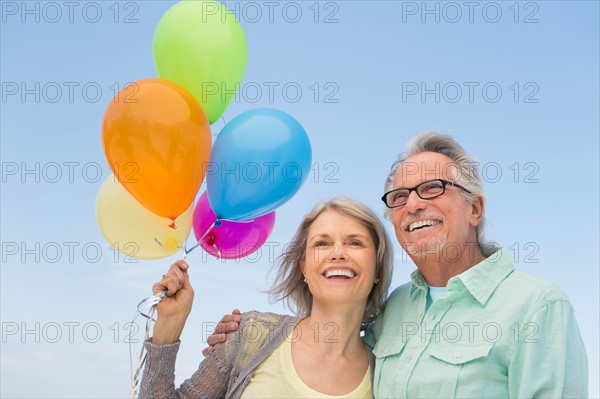 Senior couple with bunch of balloons against clear sky.