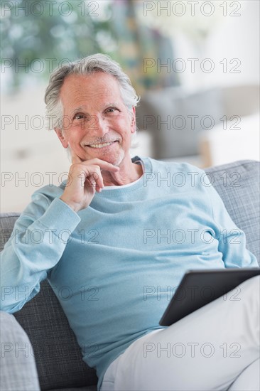 Senior man sitting on sofa with digital tablet.