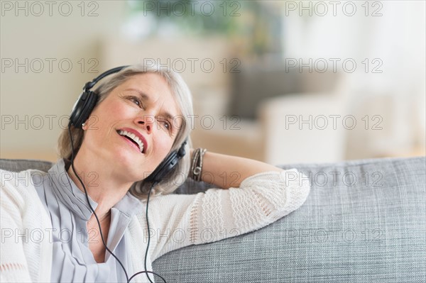 Senior woman sitting on sofa and listening to music.