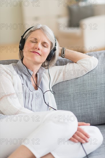 Senior woman sitting on sofa and listening to music.