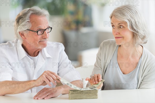 Senior couple taking money from banknotes stack.