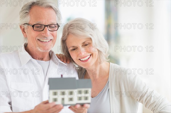 Senior couple holding model house.