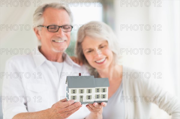 Senior couple holding model house.