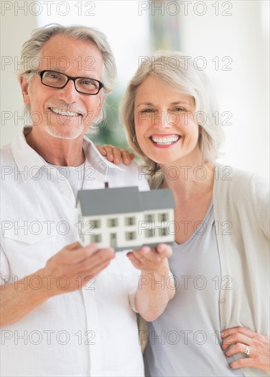 Senior couple holding model house.