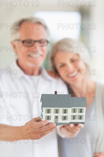 Senior couple holding model house.