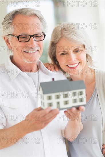 Senior couple holding model house.