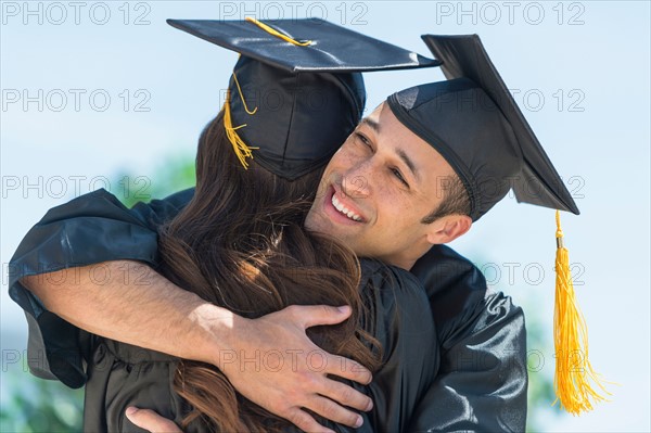 Male and female students embracing on graduation ceremony.
