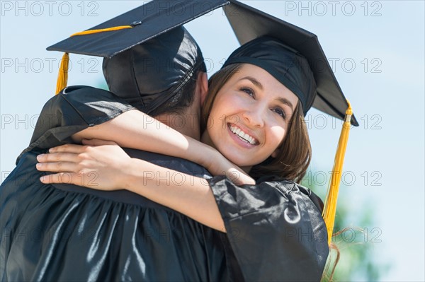 Female and male students embracing on graduation ceremony.