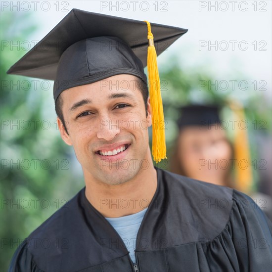 Portrait of male student on graduation ceremony with female student in background.