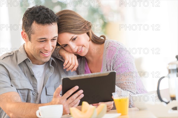 Young couple using digital tablet at kitchen table.