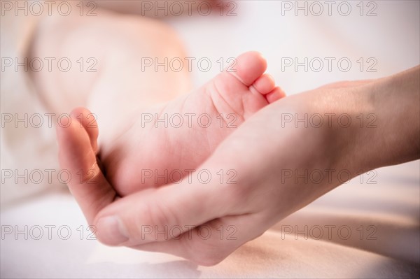 Close up of mother's hand holding tiny foot of baby girl (6-11 months)