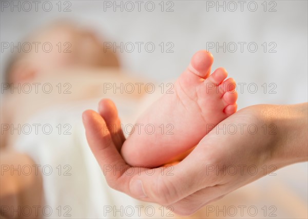 Close up of mother's hand holding tiny foot of baby girl (6-11 months)