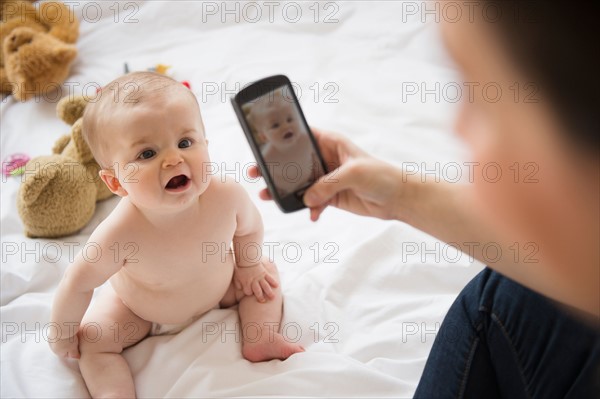 Mother photographing her baby daughter (6-11 months) with mobile phone