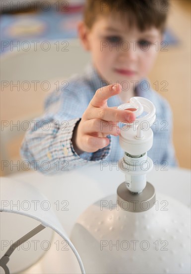 Boy (4-5) touching energy efficient lightbulb