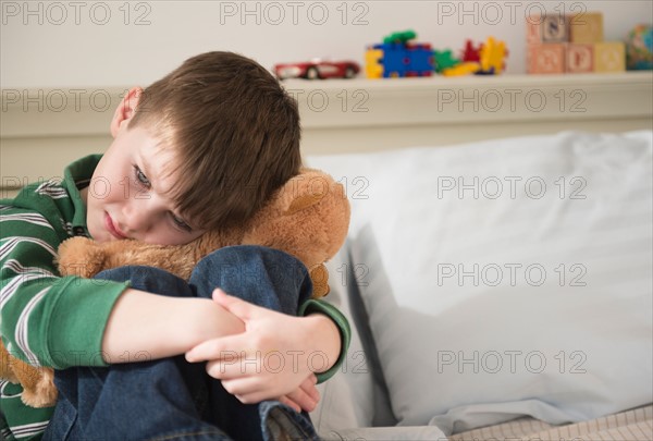 Portrait of sad boy (4-5) snuggling teddy bear