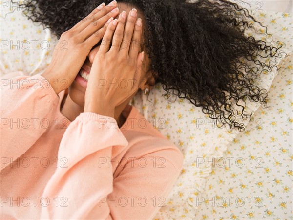 Woman lying down on bed, covering face with her hands
