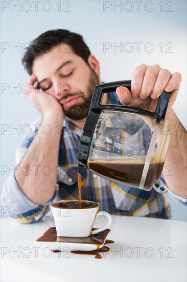 Tired, sleepy man spilling coffee on table